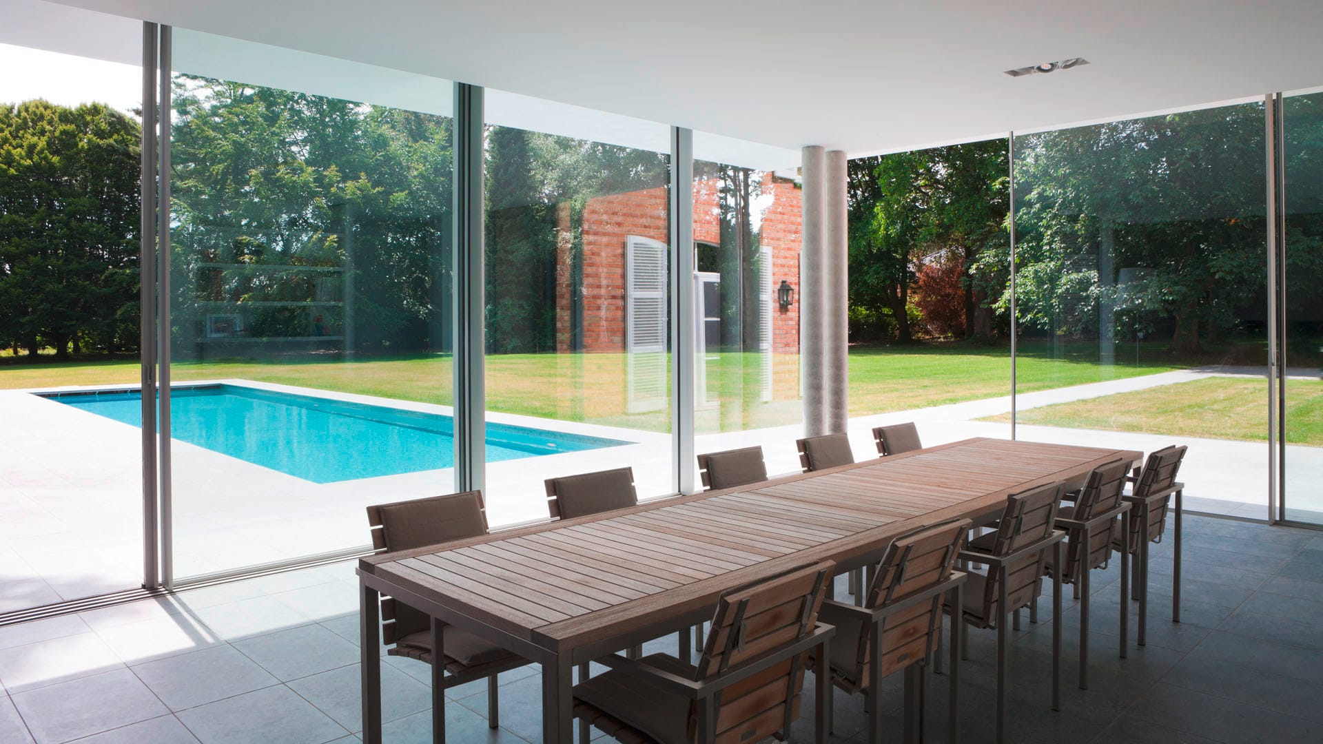 An outdoor dining terrace beside a pool and a glazed garden pavilion