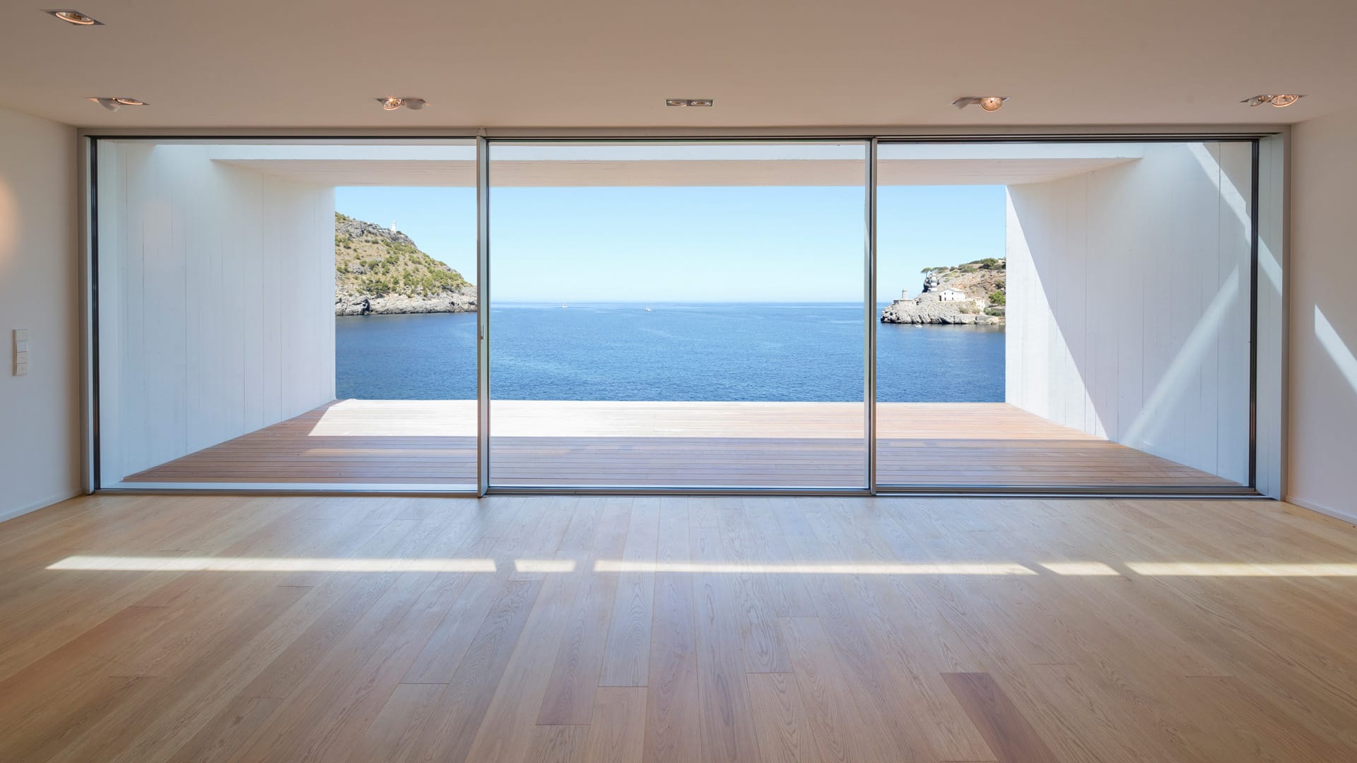 An empty room opening to a sea view through full-height slim sliding glass