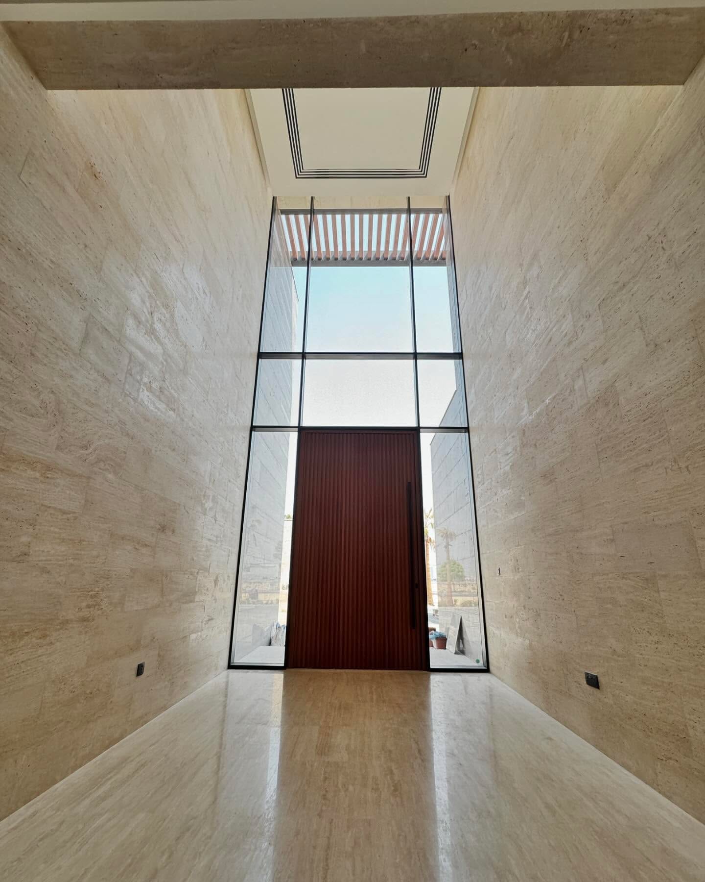 A tall glazed aluminium pivot entrance door set in a stone-lined reveal